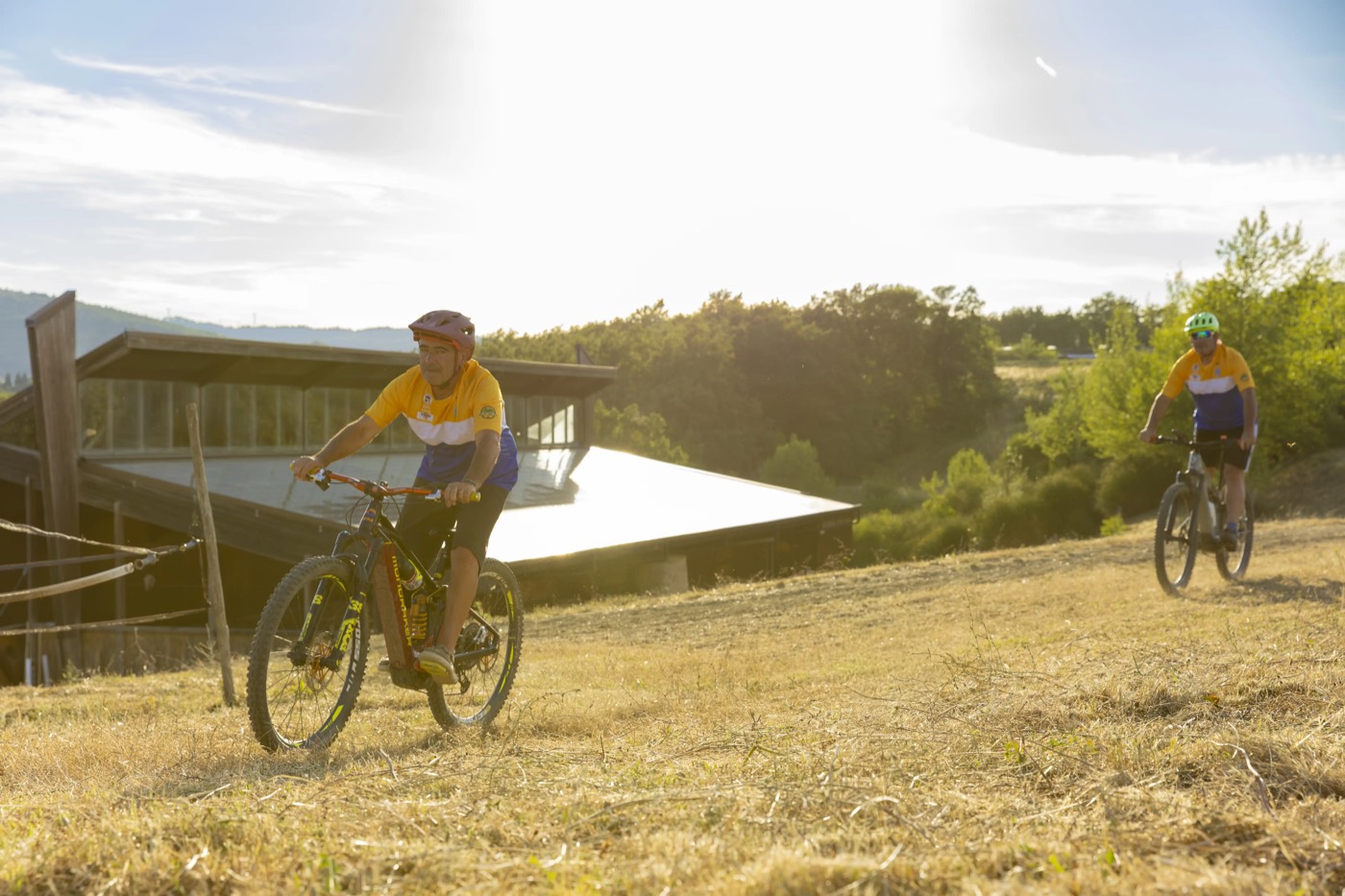 Due ciclisti attraversano un campo in controluce dorato