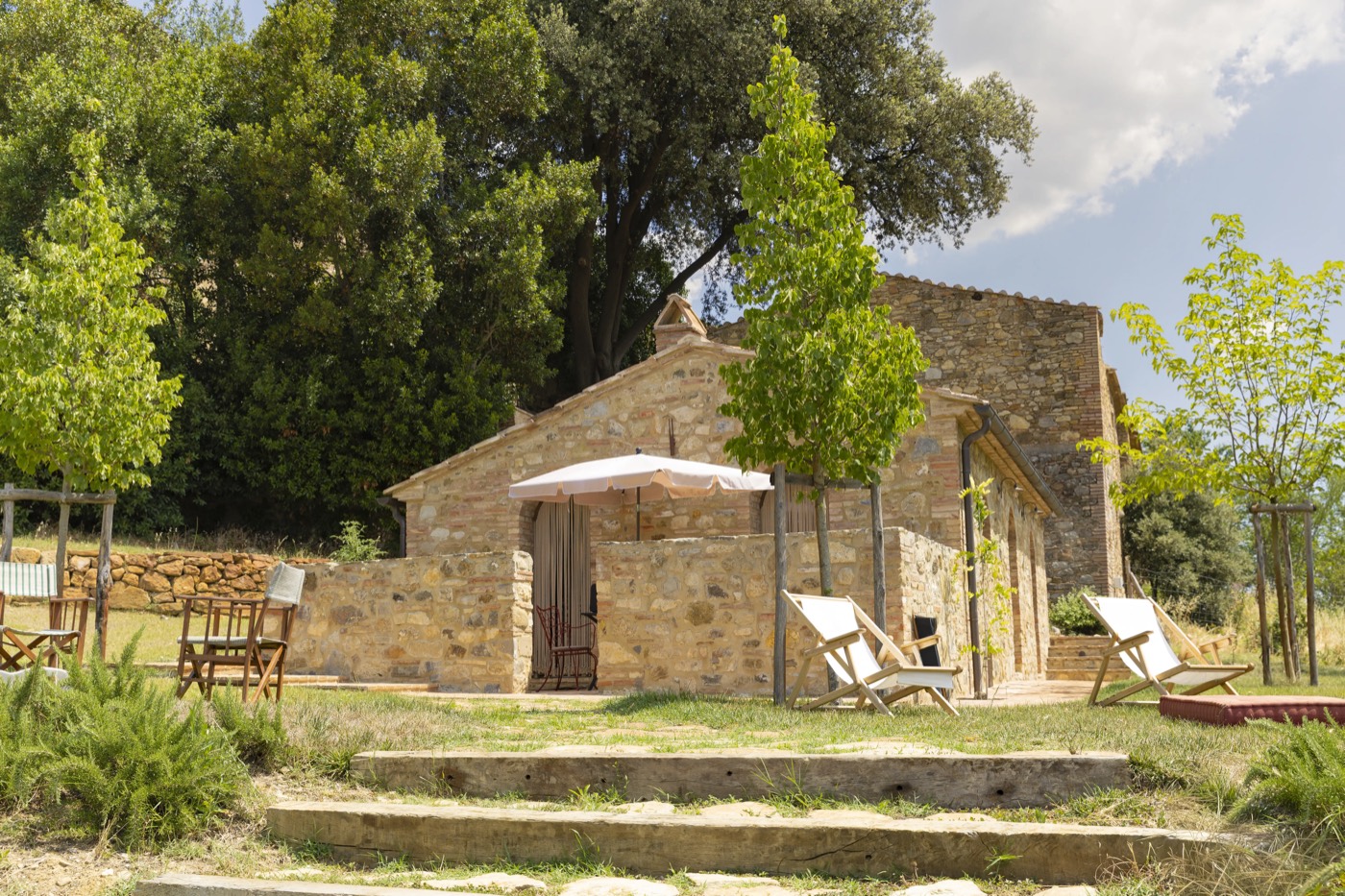 Il casolare in pietra del Podere Capannina con ombrellone, tra gli alberi